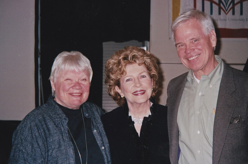 Three people stand shoulder to shoulder, smiling for the camera